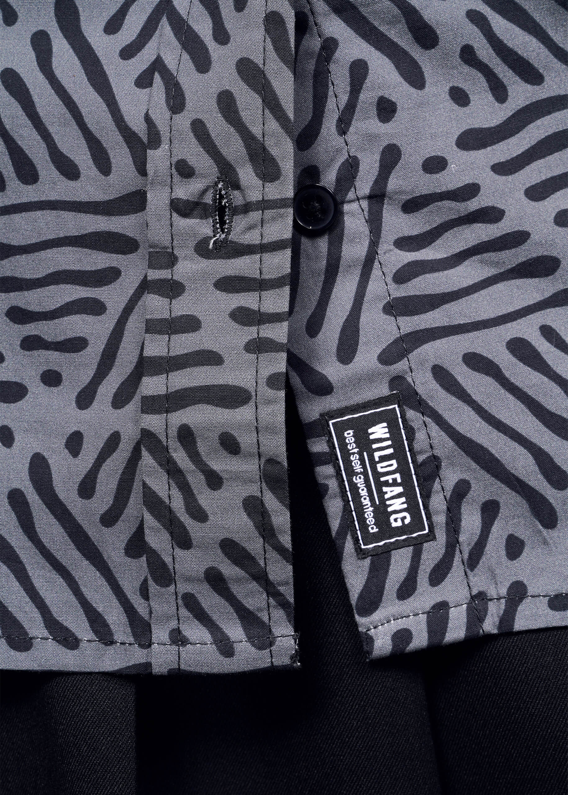 Zoom in on The Essential Convertible Sleeve Button Up, featuring a black and gray zebra print with two black buttons and a WILDFANG label that says, dont apologize. The solid black bottom layer adds depth to this versatile design.