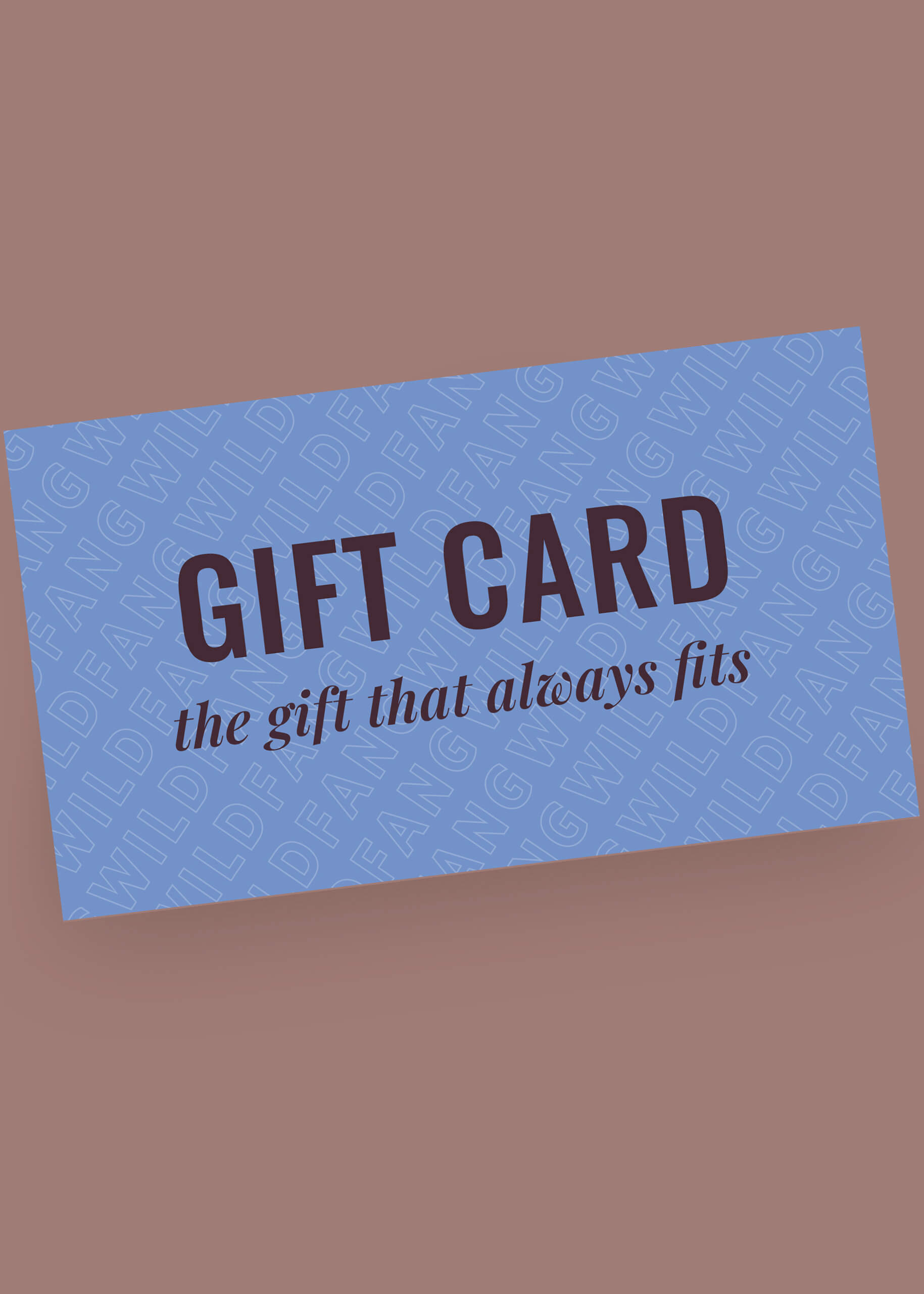 The blue Gift Card, labeled the gift that always fits, features bold black GIFT CARD text and a repeating WILDFANG background. Resting on a mauve surface, these climate-neutral cards make an ideal gift for any occasion.