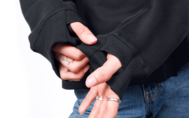 Close up of model holding cuff of the Debbie Harry x Wildfang convertible sweatshirt showing thumb hole feature.