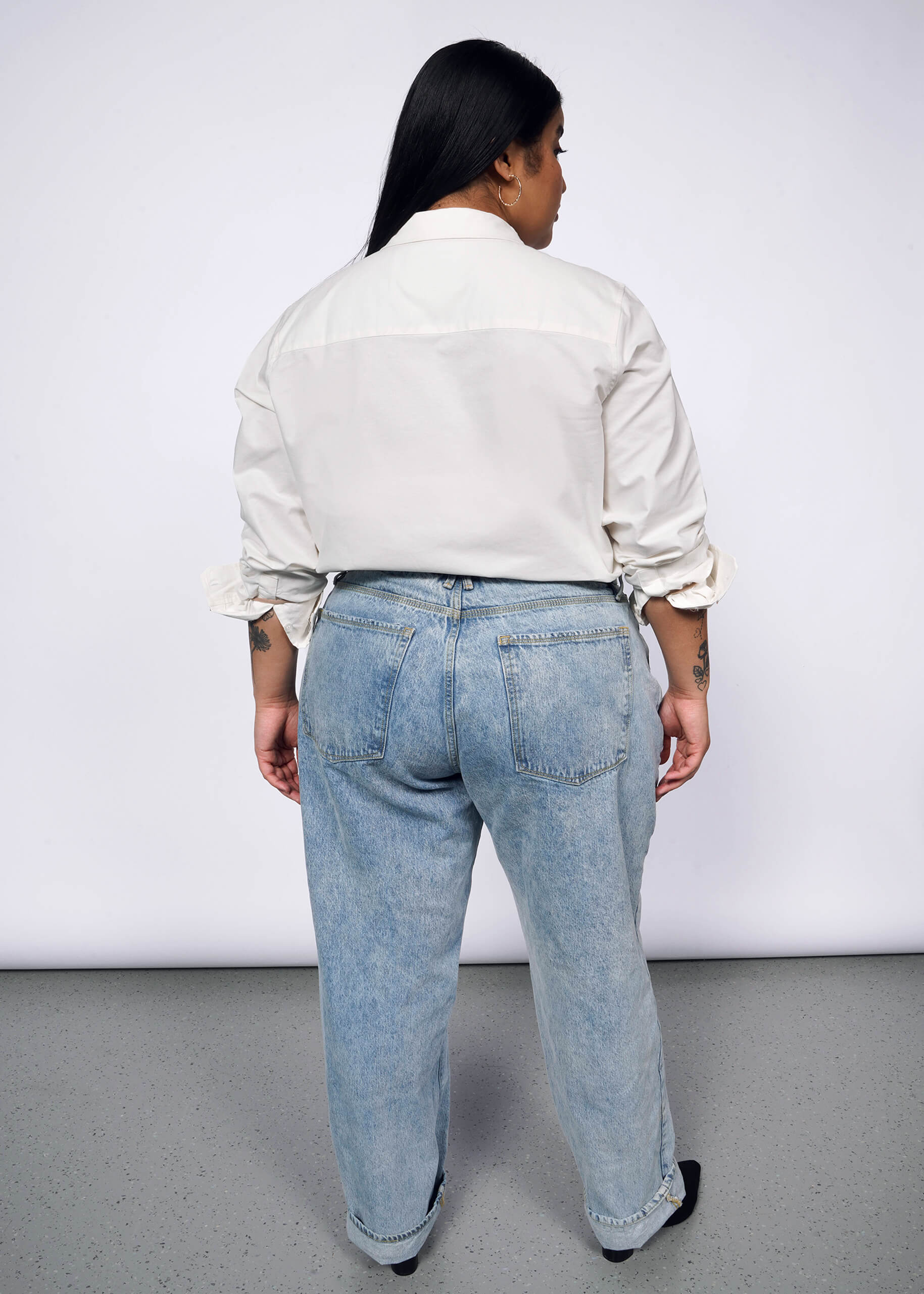 Back view of person with long black hair wearing long sleeve white button up shirt and jeans.