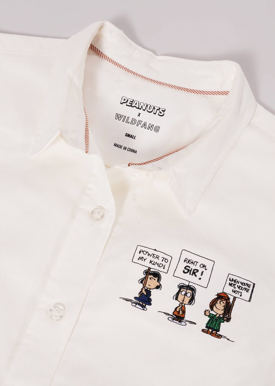 White button up laying flat on white background showing Peanuts x Wildfang logo on inside of shirt and details of embroidered Peanuts characters.