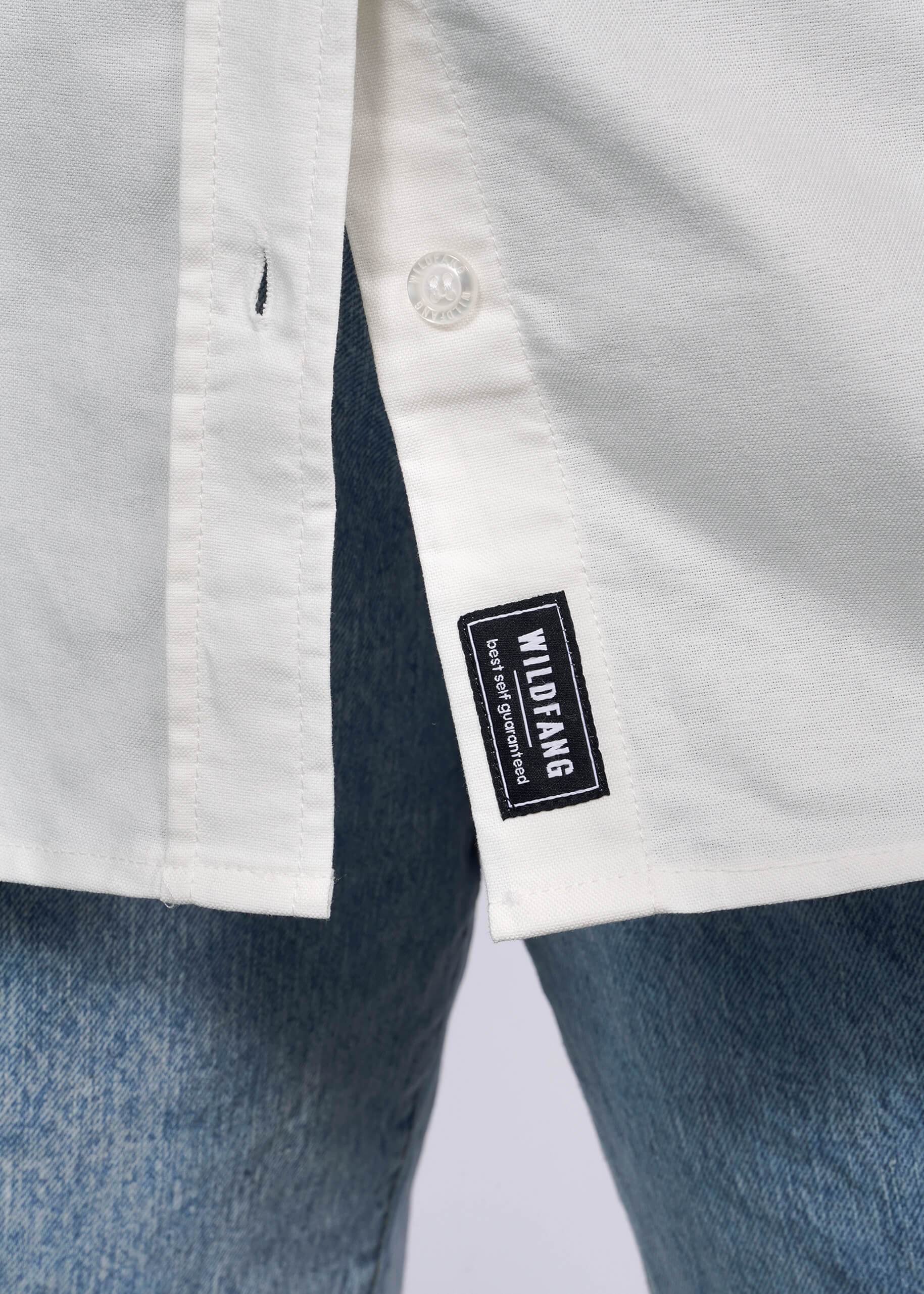 Close up of bottom hem of white button up shirt showing WILDFANG tag.