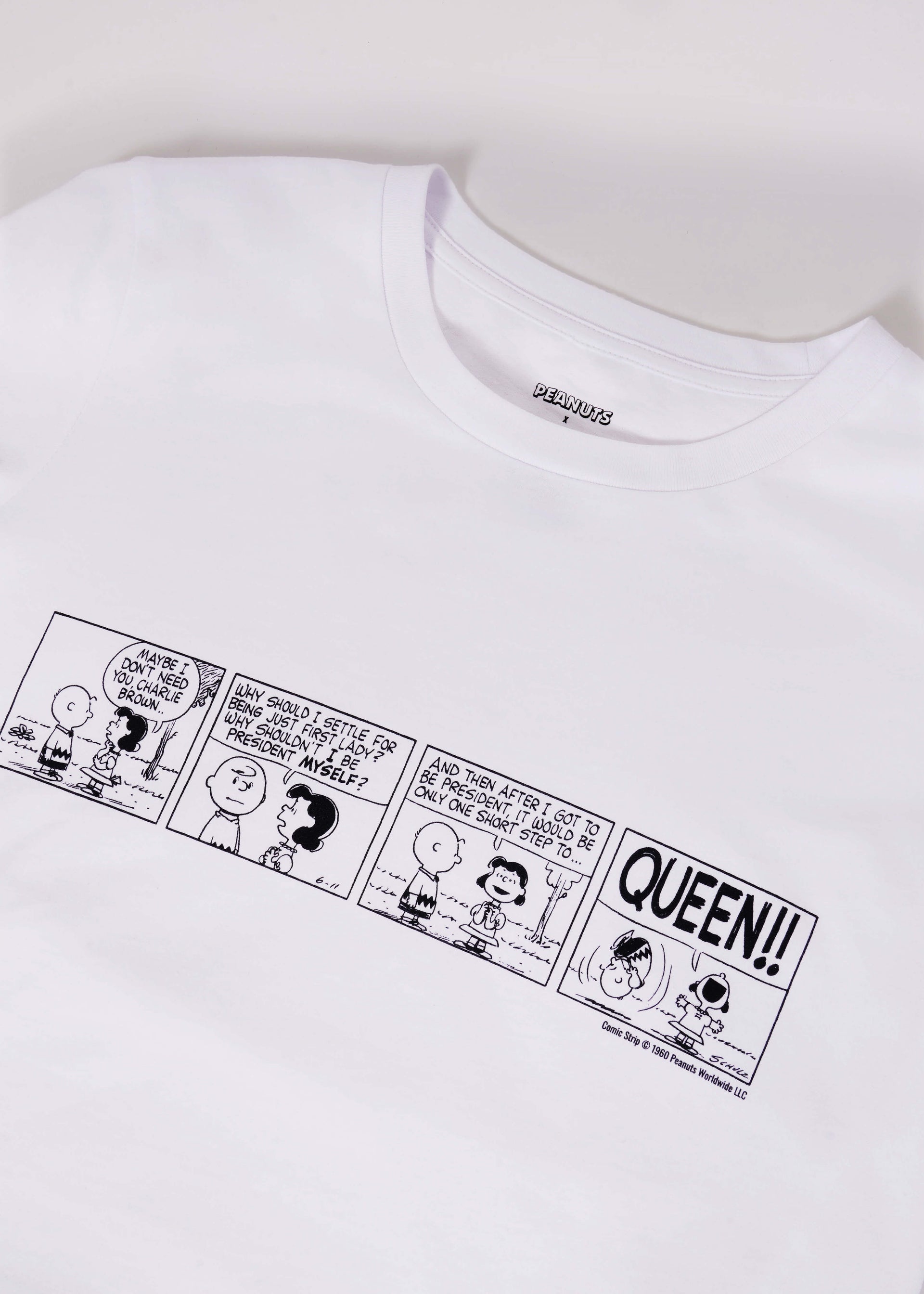 White tshirt with Peanuts comic strip printed on it lays flat on white background.