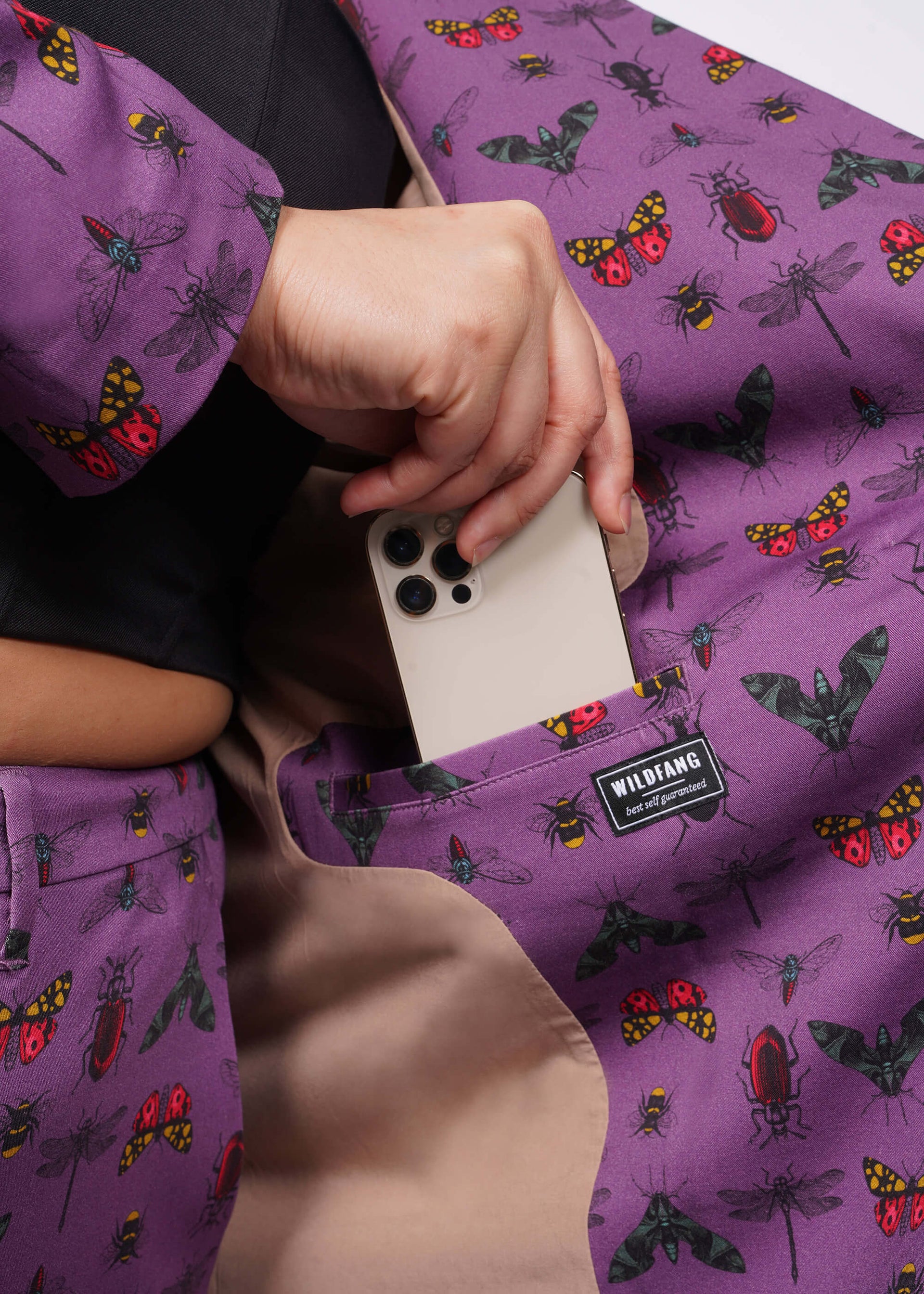 Close up of inside of purple bug printed blazer showing model putting iphone into interior pocket.