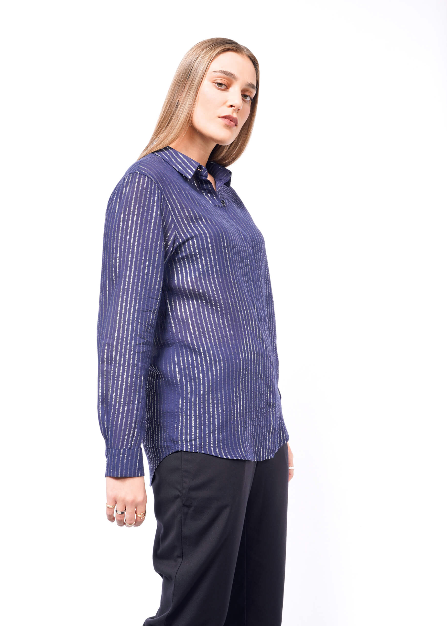 Someone with long hair wears The Empower Sheer Pinstripe Long Sleeve Button Up in blue, paired with relaxed-fit black pants. They stand against a white background, gazing at the camera with a neutral expression.