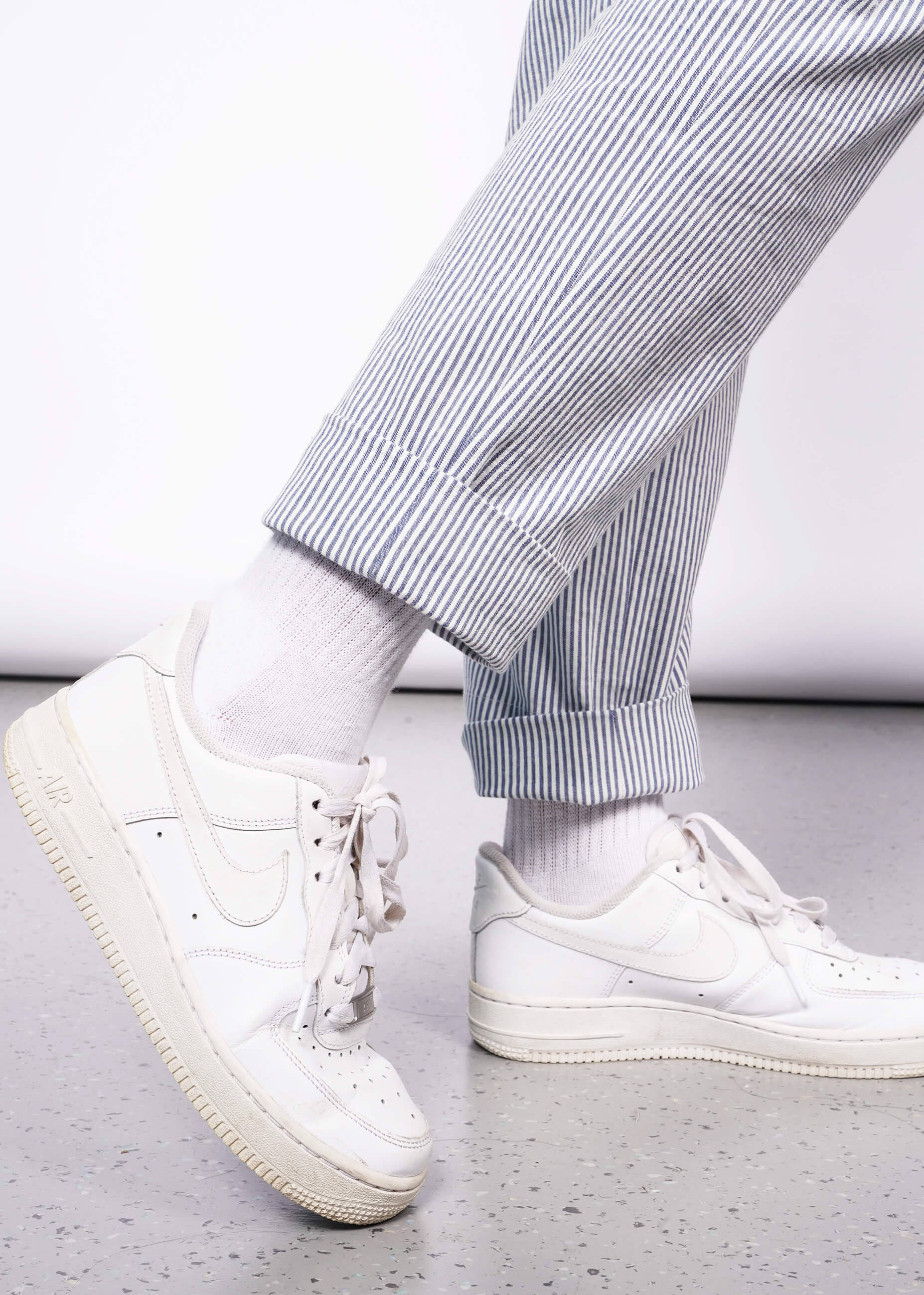 Close up view of bottom hem of seersucker blue and white pant on model wearing white sneakers.