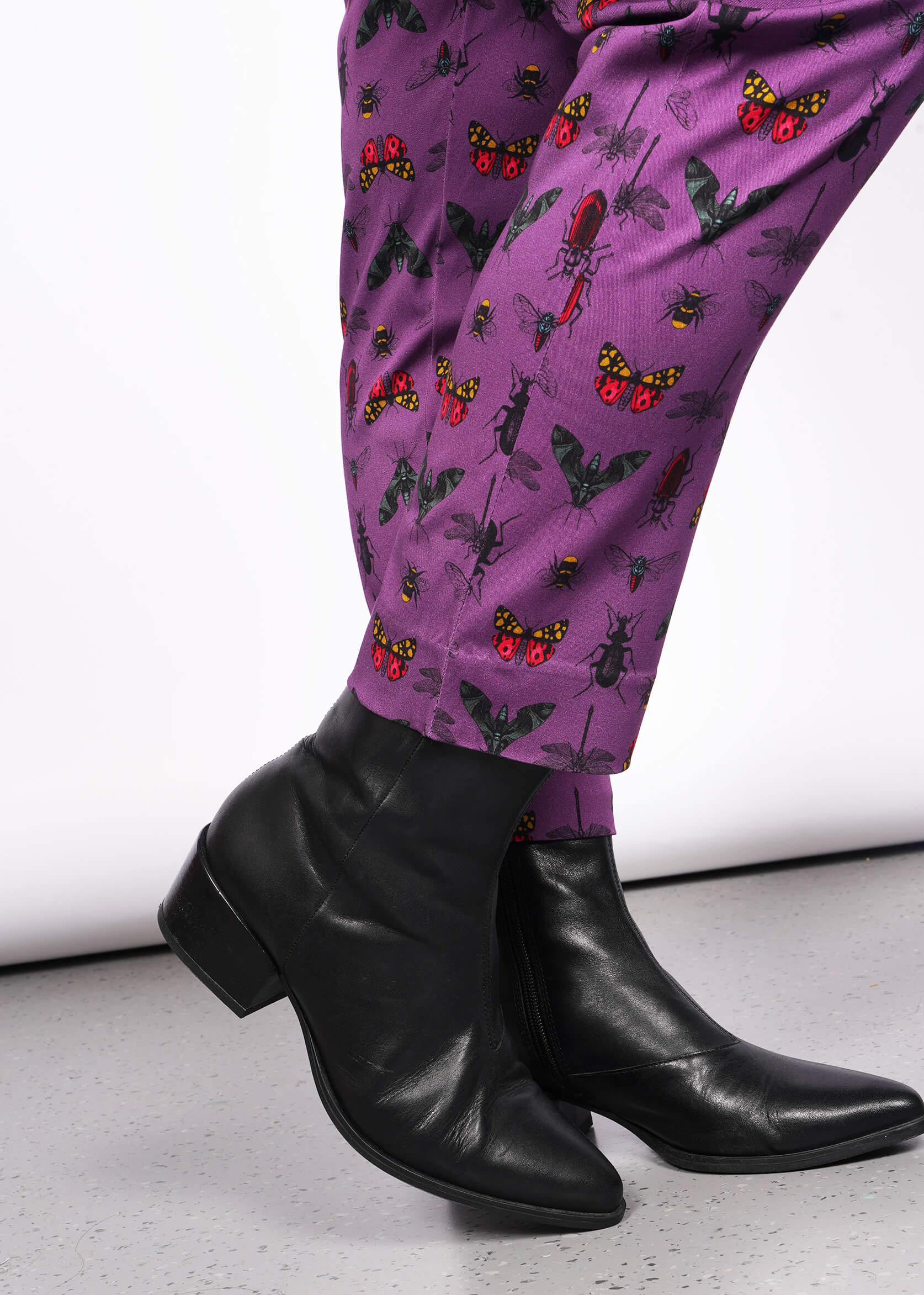 Close up view of bottom hems of purple bug printed pant. Also visible are model's black heeled boots.