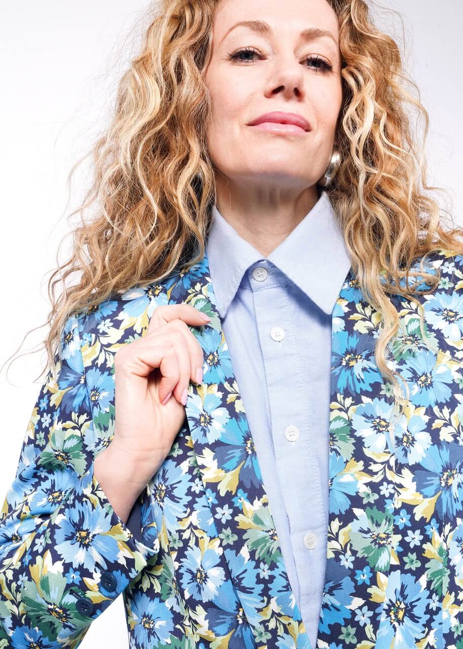 Close up of person with wavy blonde hair holding lapel of floral patterned blazer.