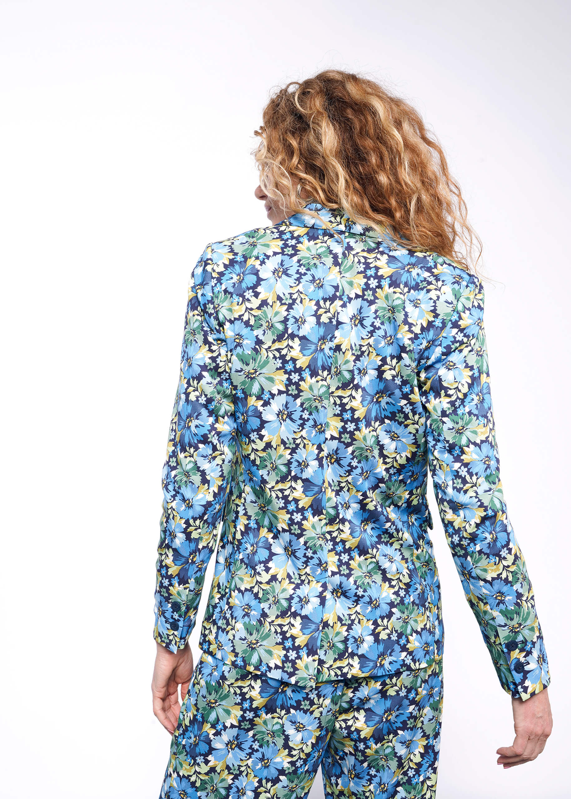 Back view of person with wavy blonde hair wearing floral patterned blazer with matching pant