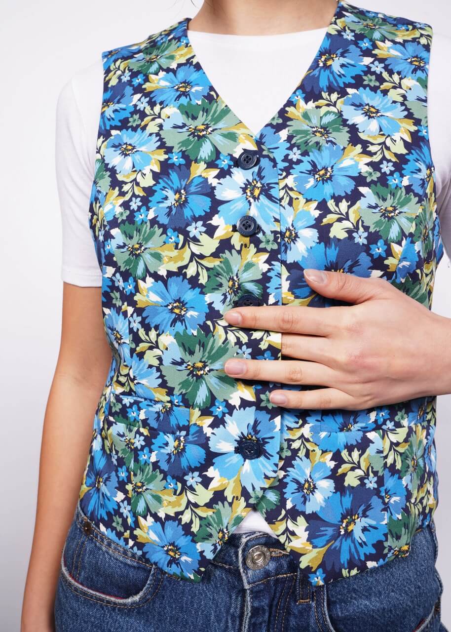 Close up of person with their fingers around the button opening of floral patterned vest over white t-shirt