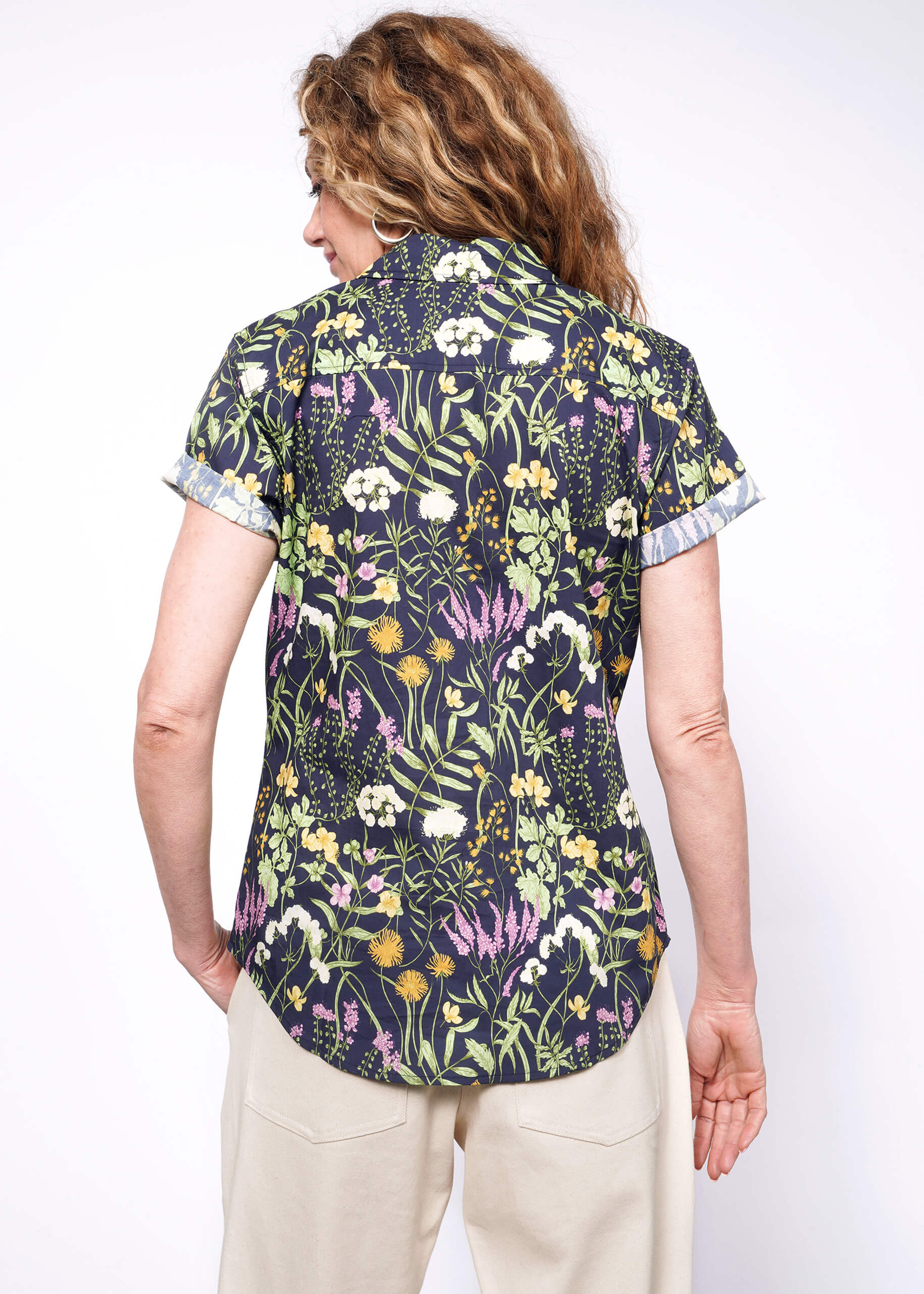 Back view of person with wavy blonde wearing short sleeve botanical printed button up shirt.