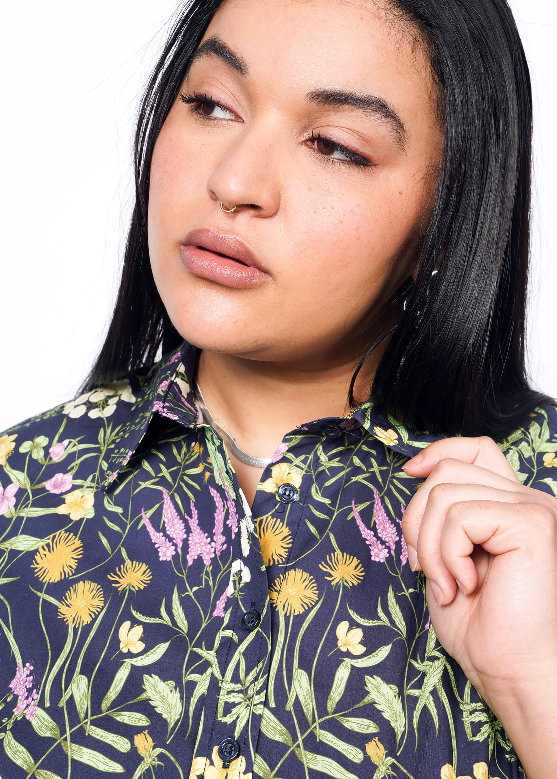 Close up of person with long black hair holding collar of short sleeve button up shirt with botanical print.