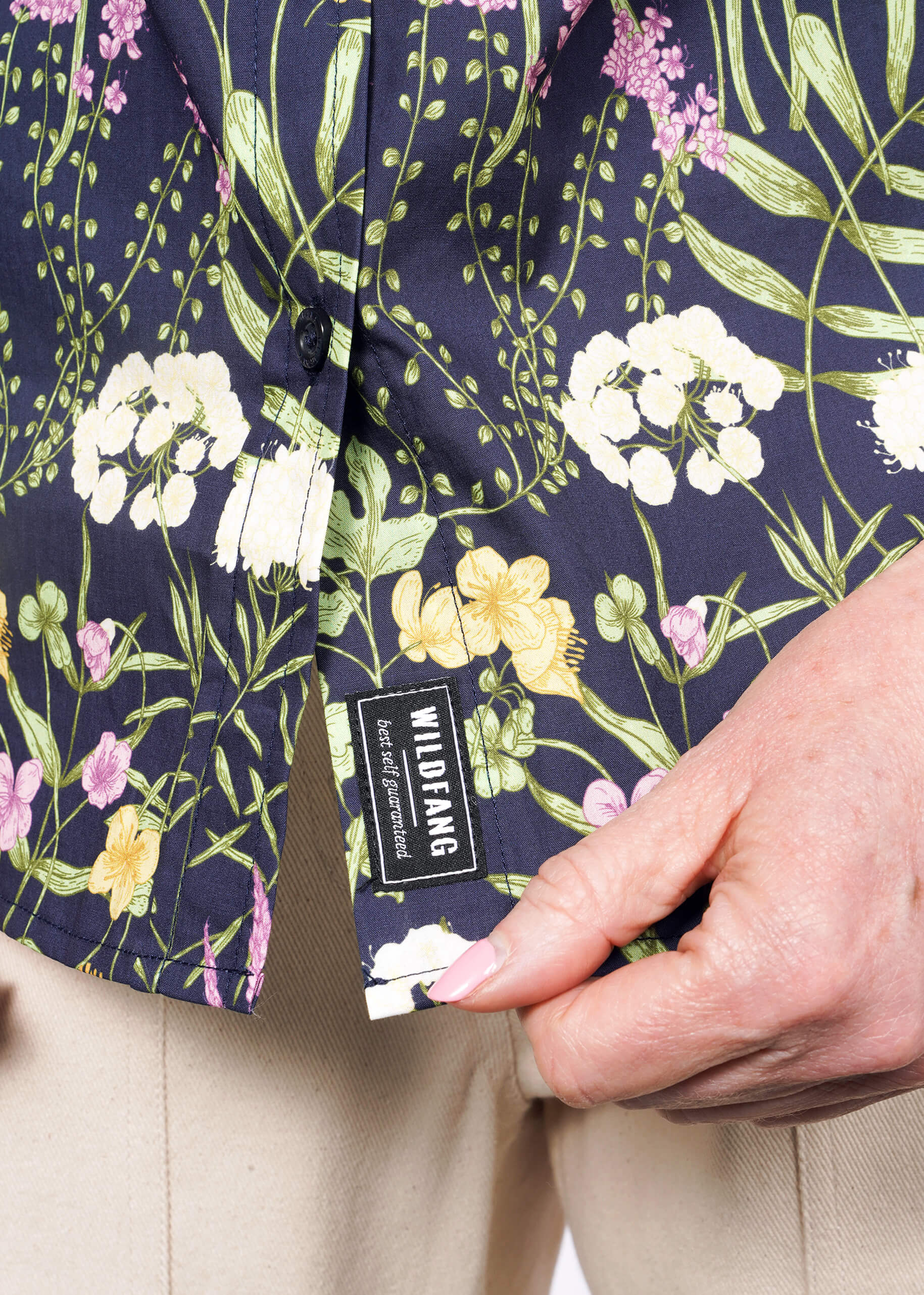 Close up of person holding bottom hem of botanical printed shirt showing WILDFANG label.