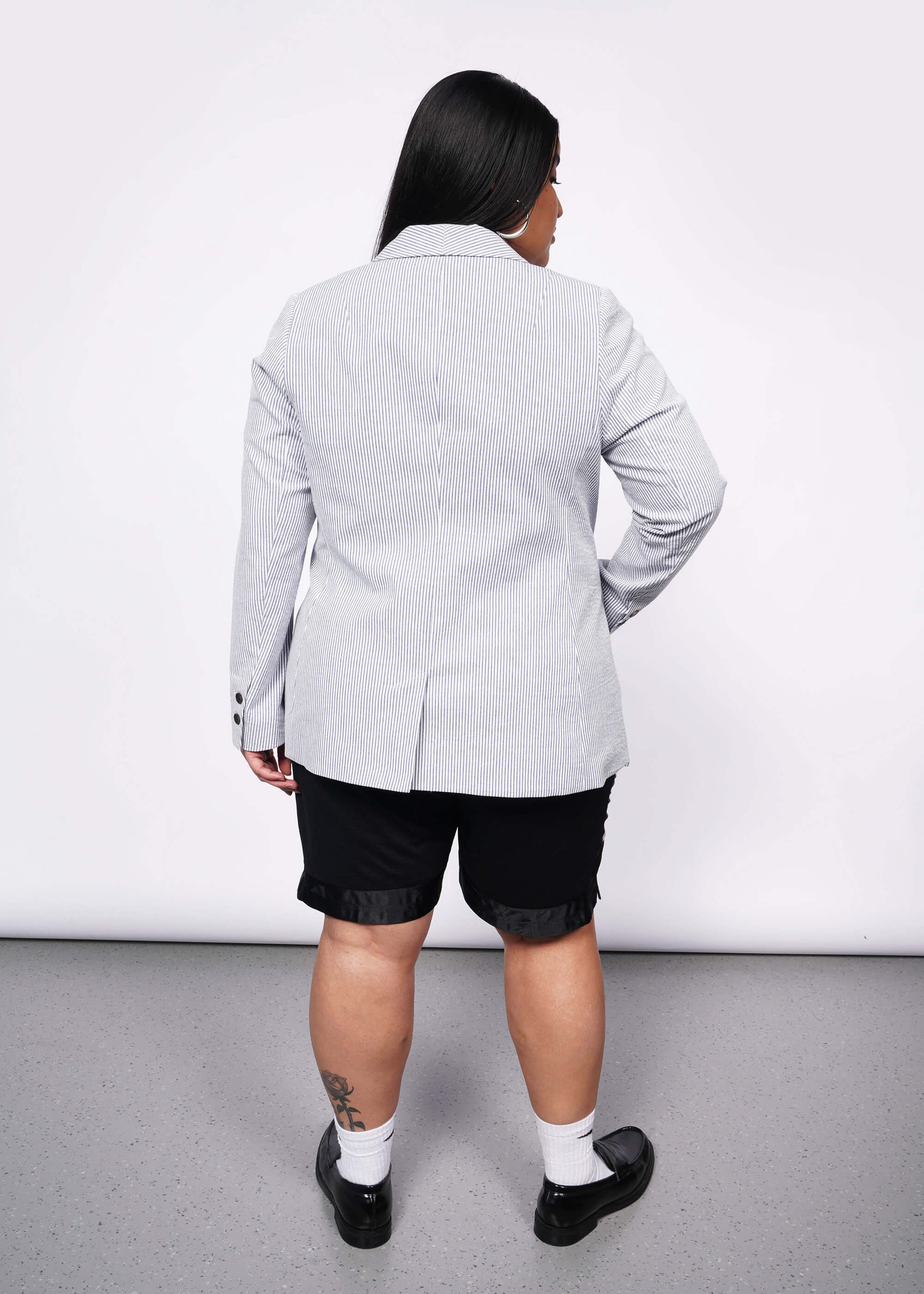 Back view of person with long black hair wears blue and white seersucker blazer and black wide leg shorts.