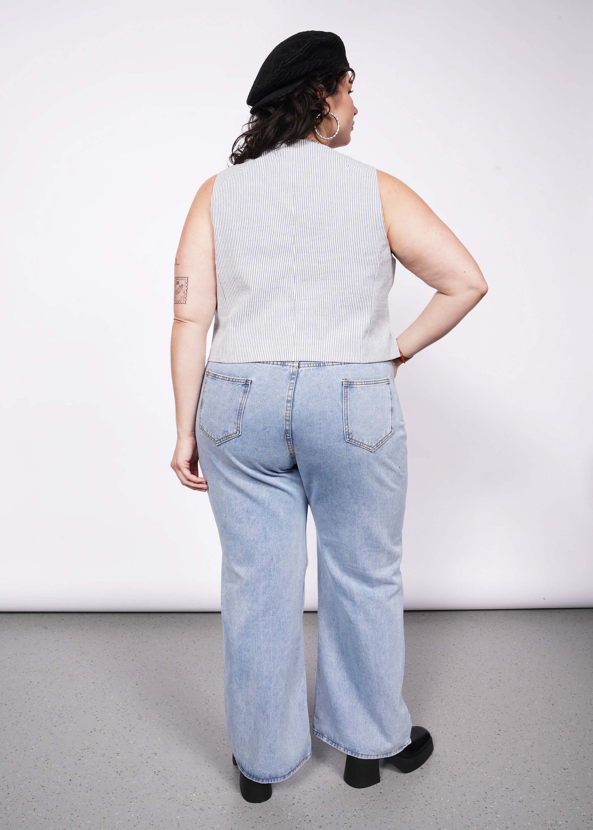 Back view of person with short curly black hair wearing seersucker blue and white vest and jeans.