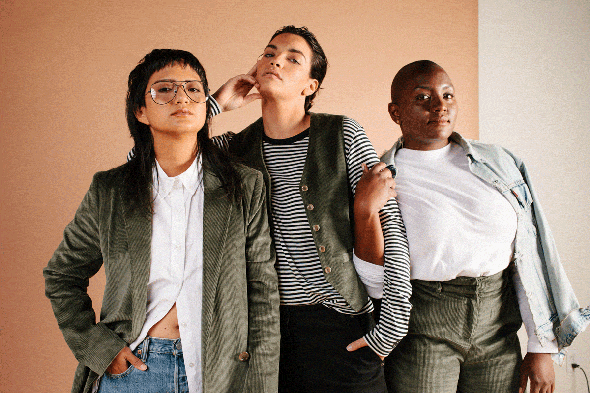 Three models stand in front of peach and white colored background wearing Wildfang suiting.