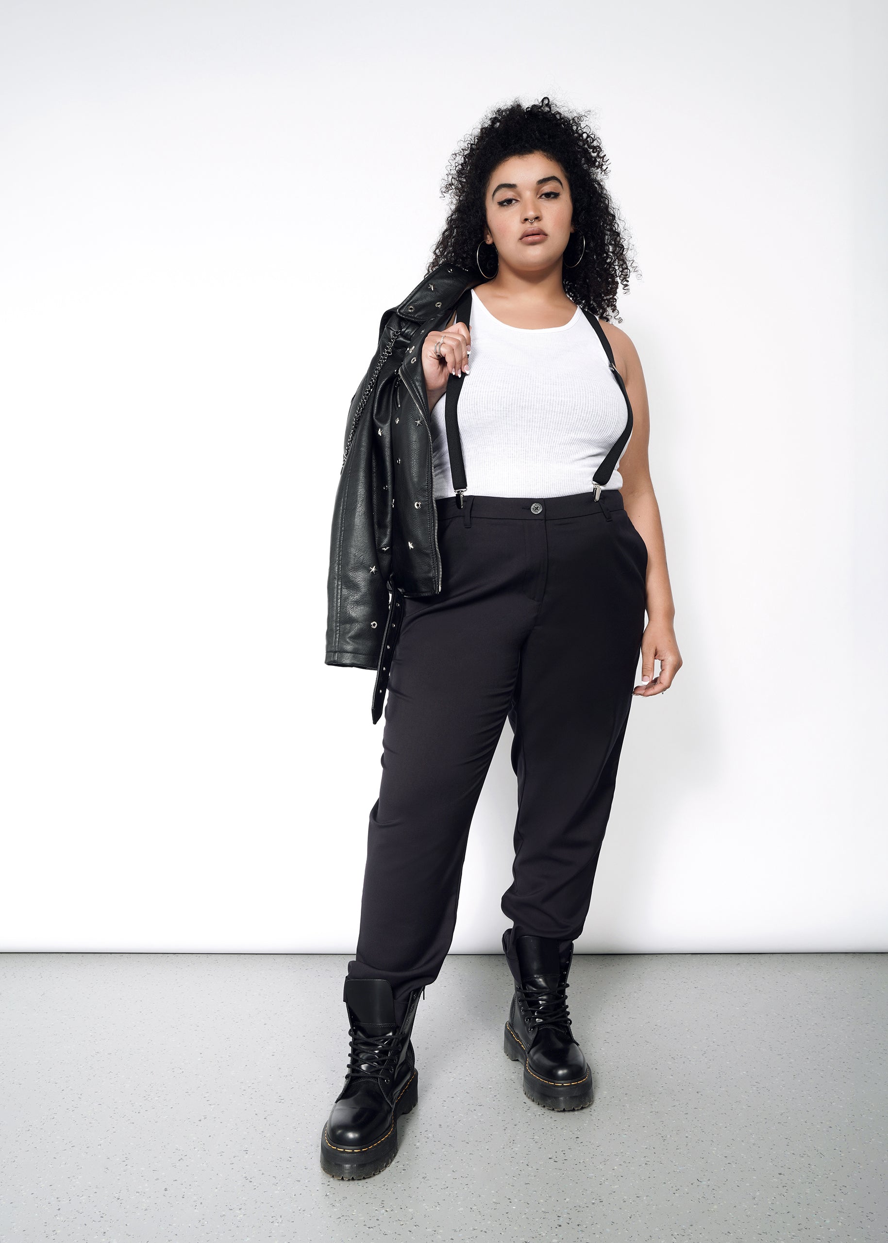 A woman wearing black wildfang pants and a leather jacket. Paired with a white tank, suspenders and doc martens